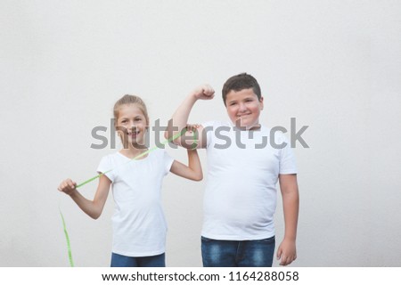 beautiful happy slim caucasian little girl measuring cute thick boy big muscle with tape