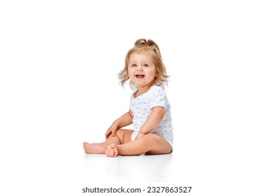 Beautiful, happy, smiling child. Little baby girl, toddler sitting on floor with joy and fun against white studio background. Concept of childhood, motherhood, care, life, birth. Copy space for ad