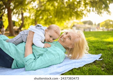 Beautiful happy smiling senior elderly woman lying on grass with cute little baby boy. Grandmother and grandson having fun time together at tropical summer day park. Multigenerational family concept - Powered by Shutterstock