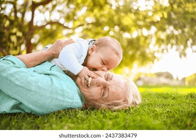 Beautiful happy smiling senior elderly woman lying on grass with cute little baby boy. Grandmother and grandson having fun time together at tropical summer day park. Multigenerational family concept - Powered by Shutterstock