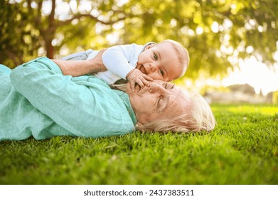 Beautiful happy smiling senior elderly woman lying on grass with cute little baby boy. Grandmother and grandson having fun time together at tropical summer day park. Multigenerational family concept - Powered by Shutterstock