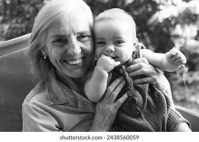 Beautiful happy smiling senior elderly woman holding on hands cute little baby boy sitting outdoor. Grandmother grandson having fun time together at sunny summer day at garden or park - Powered by Shutterstock