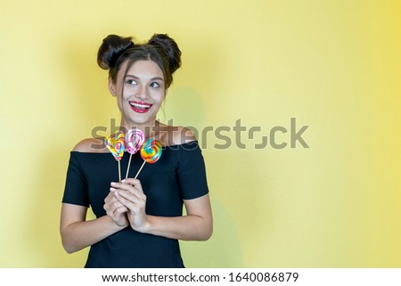 Beautiful happy smiling woman with lollipop and fashion hairstyle on yellow background. Copy space