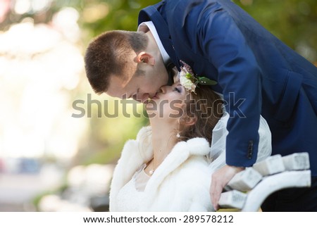 beautiful happy stylish bride with elegant groom kissing on the bench on the background of  beautiful trees in the autumn park