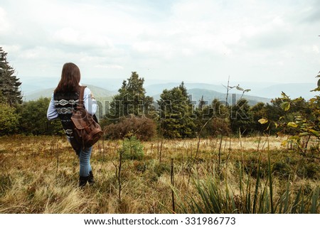 beautiful happy stylish traveling girl in the mountains on a background of a forest