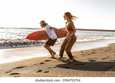 Beautiful happy surfer couple having fun on the sandy beach, running with surfboard to the waves. Summer vibes. Sunset light.  - Powered by Shutterstock