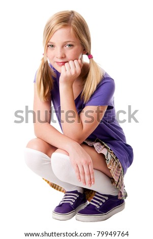 Beautiful happy teenage girl sitting squatted wearing knee socks, purple sporty shoes, shirt and colorful skirt, hand supporting her head, isolated.