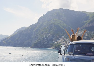 Beautiful Happy Tourist Girl Friends Enjoying Scenic View Arms Raised Of Amalfi Coast On Summer Road Trip Adventure Vacation In Vintage Van