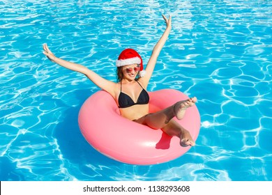 Beautiful happy woman in christmas hat with inflatable ring relaxing in blue swimming pool. - Powered by Shutterstock