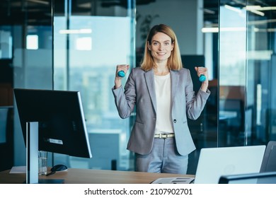 Beautiful and happy woman doing sports exercises in the office at work, during a break, business woman monitors health engaged in fitness - Powered by Shutterstock