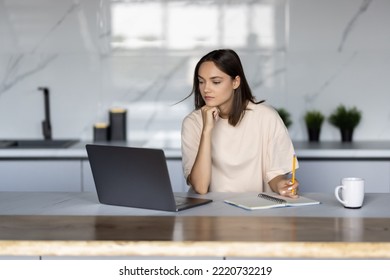 Beautiful happy woman drinking tea while working with laptop in cozy kitchen