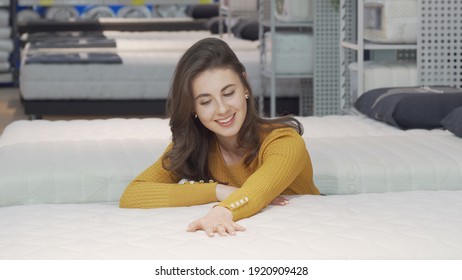 Beautiful Happy Woman Examining Orthopedic Mattress On Sale. Cheerful Female Customer Choosing New Bed And Mattress To Buy At Furnishings Store. Bedding Concept