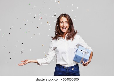 Beautiful happy woman with gift box at celebration party with confetti falling everywhere on her. Birthday or New Year eve celebrating concept - Powered by Shutterstock