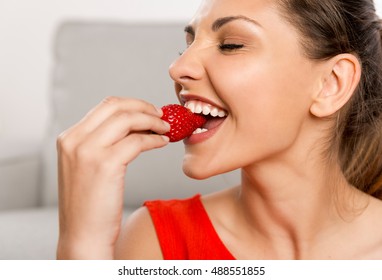 Beautiful happy woman at home eating a strawberries