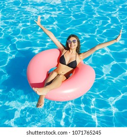 Beautiful happy woman with inflatable ring relaxing in blue swimming pool.