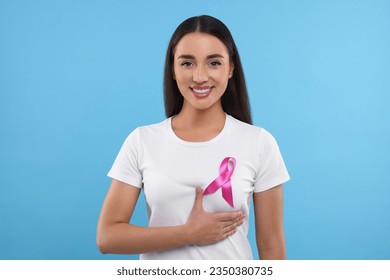 Beautiful happy woman with pink ribbon on light blue background. Breast cancer awareness - Powered by Shutterstock