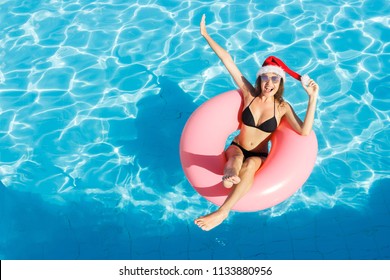 Beautiful happy woman in Santa Claus hat with inflatable ring relaxing in blue swimming pool. - Powered by Shutterstock