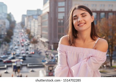 Beautiful happy woman smiling with her eyes closed, enjoying warm autumn sun outdoors on city streets, copy space. Travel, tourism concept