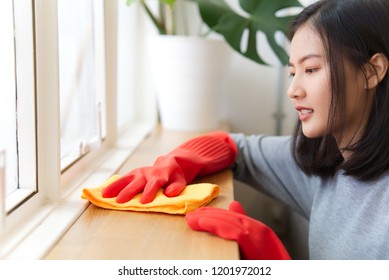 Beautiful Happy Young Asian Woman Is Using A Cloth Wiping Out Dust On The Wooden Counter. She Has Smiley Face While Cleaning The House. Happy Cleaning Concept.