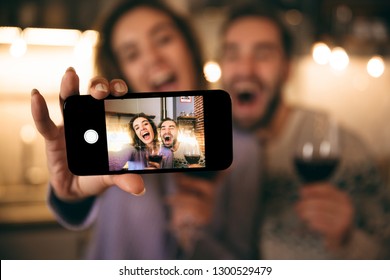 Beau jeune couple heureux passant une soirée romantique à la maison, buvant du vin rouge, prenant un selfie : photo de stock