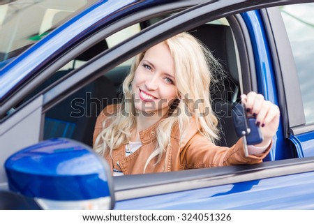 Beautiful happy young girl sitting in her car showing car key