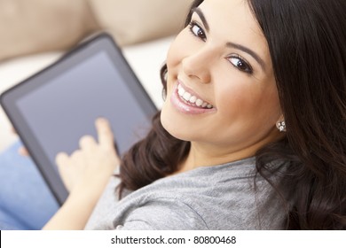 Beautiful Happy Young Latina Hispanic Woman Smiling And Using A Tablet Computer At Home On Her Sofa