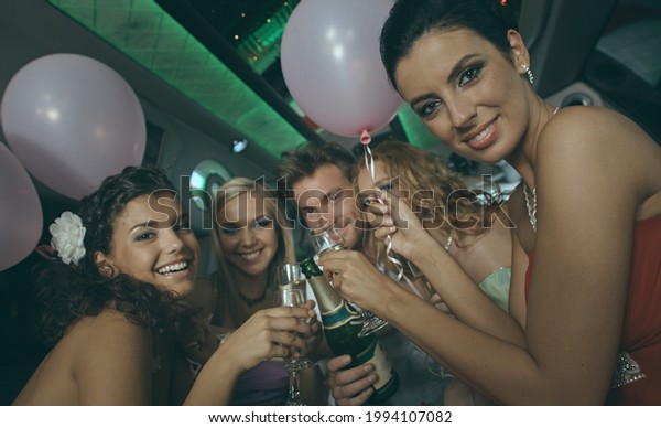 Beautiful happy young\
people on party in luxury limousine clinking with champagne\
glasses, celebrating.