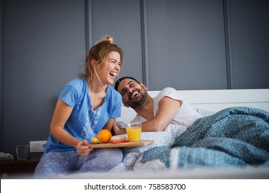 Beautiful happy young romantic girl brings breakfast to her husband in the bed and laughing together after he wakes up. - Powered by Shutterstock