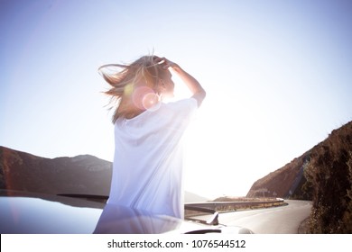 Beautiful And Happy Young Woman, Full Of Emotions And Feelings Enjoys Warm Summer Air And Sunshine On Sunny Day, Stands Up In Car Out Of Convertible Cabriolet, Wind In Hair Full Of Freedom