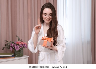 Beautiful happy young woman holding gift box in room