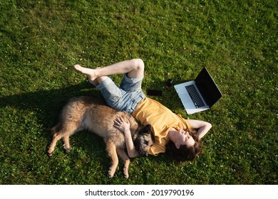 Beautiful Happy Young Woman Lying On The Grass With Laptop And Dog, Shot From Above