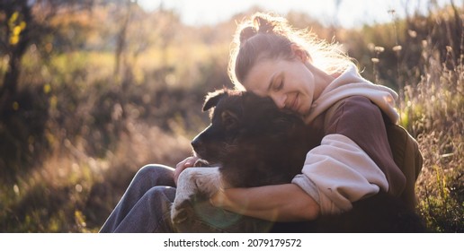 Beautiful happy young woman sitting on the grass hugging a dog. Love and affection for pets, friendship companion