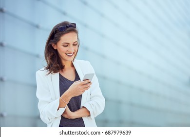 Beautiful happy young woman texting and smiling in modern outside setting