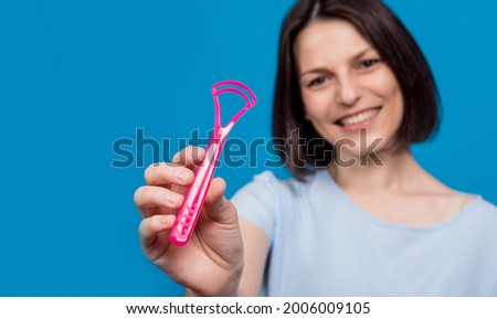Beautiful happy young woman with tongue scraper on blank blue background