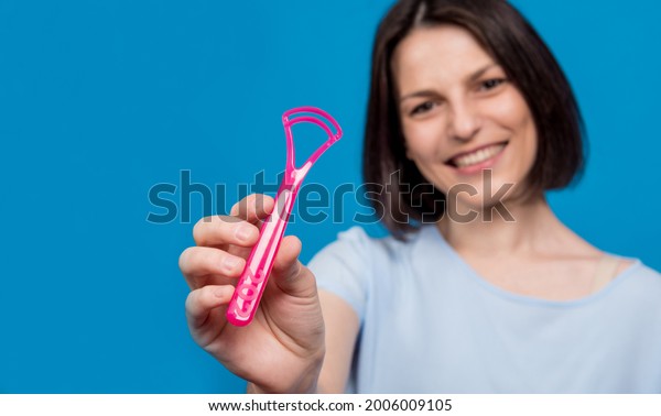 Beautiful happy young woman with tongue\
scraper on blank blue\
background