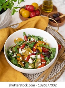 Beautiful, healthy, colorful salad from roasted red and yellow peppers, grilled zucchini, cherry tomatoes, olives and feta cheese. Served in a white round bowl on a golden metal tray. Front view. 