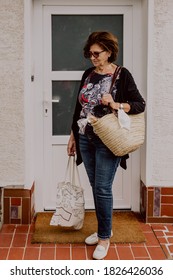 Beautiful And Healthy Looking Senior Woman In Her 70s Holding Tote Bags From Grocery Shopping During Coronavirus Days, Used Face Mask Hanging Around Her Hand. Covid-19 And Senior Citizen