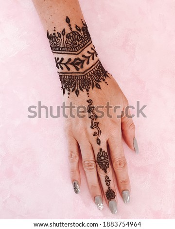beautiful henna tattoo on the wrist and hand with pink background
