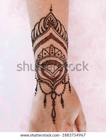 beautiful henna tattoo on the wrist and hand with pink background