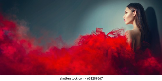Beautiful High fashion woman in red dress posing in studio. Gorgeous brunette model girl with beautiful hairstyle and make-up, Wearing Stunning evening red dress with long gown of tulle and smoke