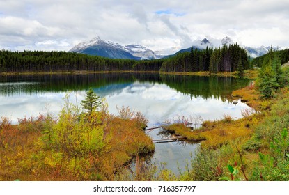 Beautiful high mountains of the Canadian Rockies reflecting in an alpine lake along the Icefields Parkway between Banff and Jasper during foliage season with changing yellow, green and red leaves