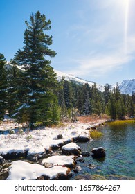 Beautiful highland mountain lake with fir forest on the shore and snow covered mountain range in distance