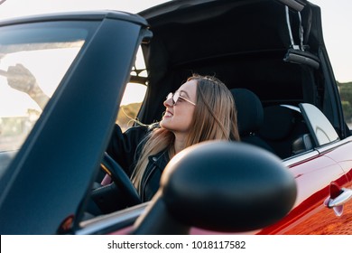 Beautiful and hip young blonde woman or teenager, hipster or millennial sits inside convertible car and opens electronical button roof top of cabriolet. First vehicle and driving license practice