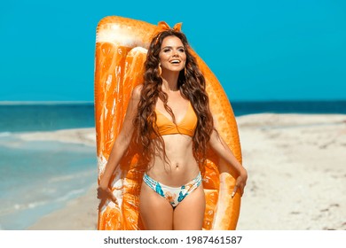 Beautiful hippie girl portrait by orange Inflatable pool float mattress on tropical beach. Fit Brunette with long healthy curly hair and makeup on summer vacation. - Powered by Shutterstock