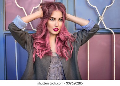 Beautiful hipster fashion model with curly pink hair posing in front of the colorful wall