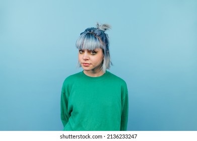 Beautiful hipster girl in a green sweater and with blue hair isolated on a blue background looking at the camera with a serious face. - Powered by Shutterstock