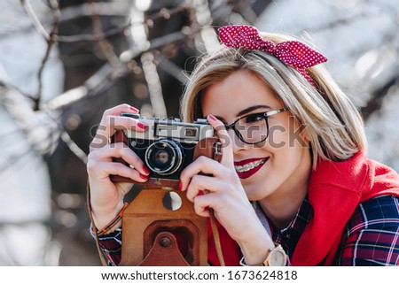 Beautiful hipster woman with braces using unknown vintage analog camera. Wearing red toned clothes with neutral color background. photographer