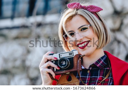 Beautiful hipster woman with braces using unknown vintage analog camera. Wearing red toned clothes with neutral color background. photographer
