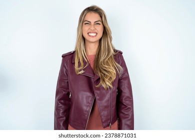 Beautiful hispanic blonde businesswoman wearing leather jacket keeps teeth clenched, frowns face in dissatisfaction, irritated because of much duties.