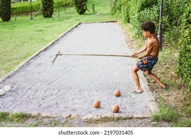 Beautiful Hispanic Boy Raking The Ground To Play Bocce Ball